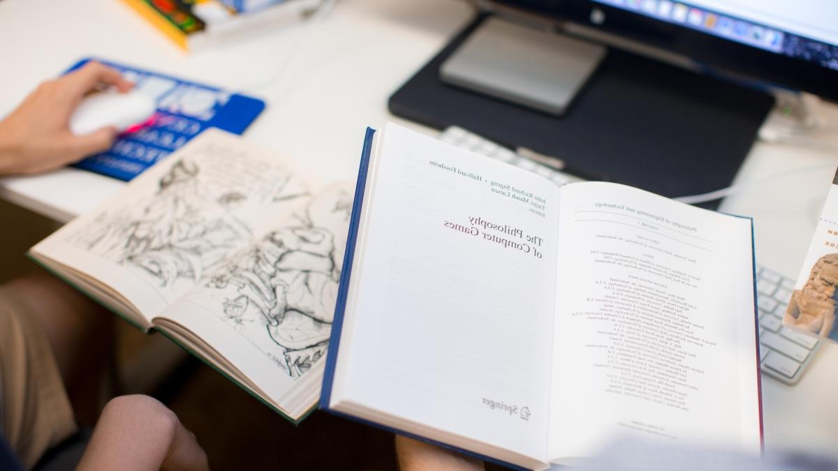 philosophy books lie open on a desk in front of a computer screen